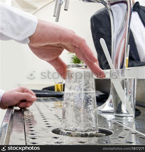 a bartender rinsing a beerglass at his bar with customers at the background