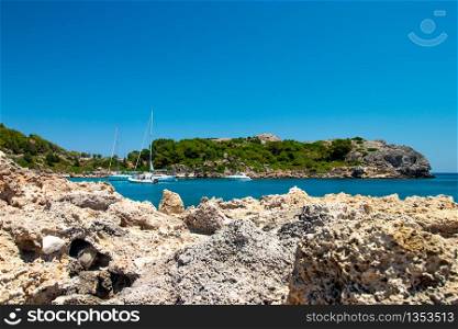 A bay on the island of Rhodes with sailing ships and rocks in the foreground