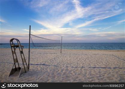 A beach volleyball net on the sandy tropical beach at the sunset / sunrise