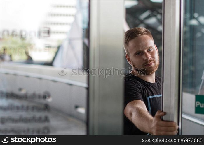 A bearded man opening glass door and looking straight on camera