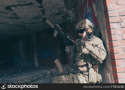 A bearded soldier in special forces uniform in a dangerous military mission, refile his weapon while hiding from the wall. Selective focus. High-quality photo. A bearded soldier in special forces uniform in dangerous military mission, refile his weapon while hiding from the wall. Selective focus 