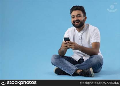 A BEARDED YOUNG MAN SITTING AND HAPPILY USING MOBILE PHONE