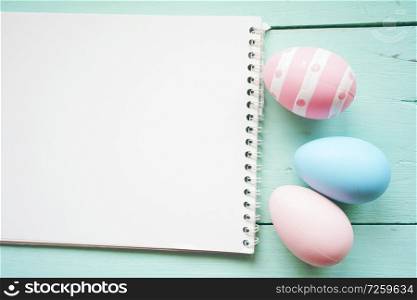 A beautiful and colorful close-up flat of isolated easter eggs in plain colors and striped by a notebook over a pastel blue wooden table with space