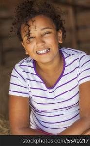 A beautiful and happy mixed race African American female girl child smiling sitting in hay filled barn