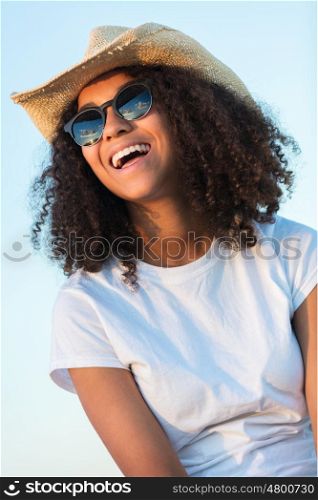 A beautiful and happy mixed race African American female girl child teenager young woman in sunshine wearing sunglasses and straw cowboy hat smiling with perfect teeth