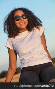 A beautiful and happy mixed race African American female girl child teenager young woman in sunshine wearing sunglasses and smiling with perfect teeth
