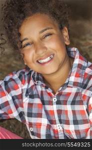 A beautiful and happy mixed race African American female girl child wearing a plaid shirt sitting in hay filled barn