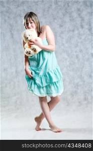 A beautiful and sexy 20-25 years blond girl with teddy bear in dress on grey background