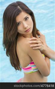 A beautiful and sexy young Chinese Asian woman wearing a bikini in a turquoise blue swimming pool. Spa, healthy living and health club concept.