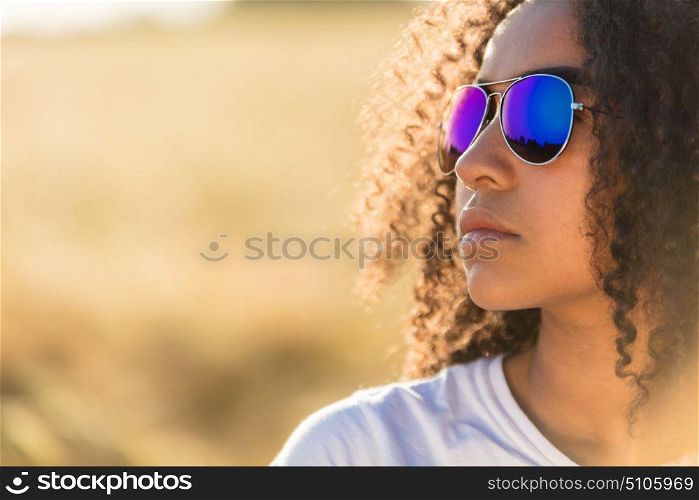 A beautiful and thoughtful mixed race African American female girl child teenager young woman in sunshine wearing blue reflective aviator sunglasses