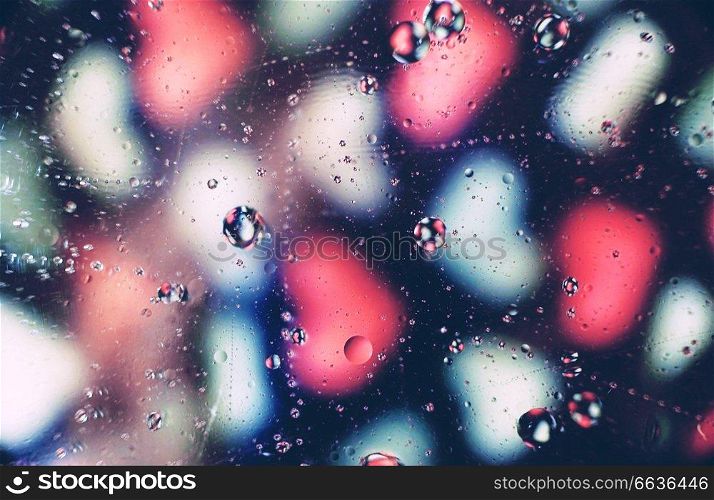 A beautiful and vibrant macro of oil bubbles on water with a blur of white and pink hearts pattern on black background