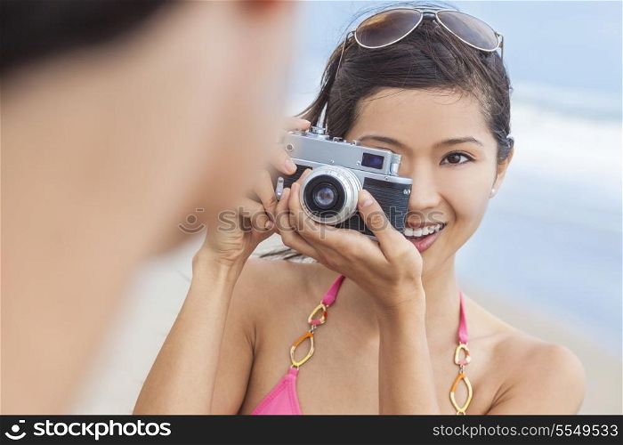 A beautiful Asian Chinese girl or young woman wearing bikini at a beach looking happy taking pictures or photographs with a retro digital camera
