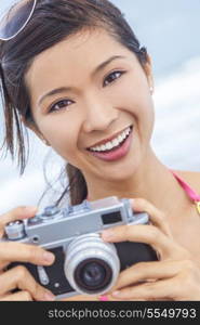 A beautiful Asian Chinese girl or young woman wearing bikini at a beach looking happy taking pictures or photographs with a retro digital camera