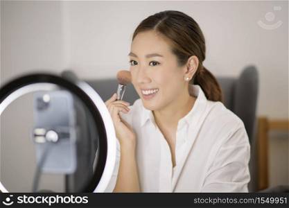 A beautiful Asian makeup blogger is live streaming how to beauty face makeup in her home, beauty and technology concept . . A beautiful Asian makeup blogger is live streaming how to beauty face makeup in her home, beauty and technology concept