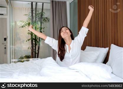A beautiful asian woman do stretching after waking up in the morning on a white cozy bed at home