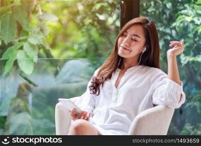 A beautiful asian woman enjoy listening to music with phone and earphone at home , green nature background , happiness and relaxation concepts