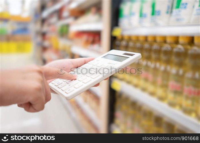 A beautiful Asian woman holding a calculator to calculate the cost and price reduction in a supermarket. Concept of price reduction, saving and value