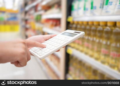 A beautiful Asian woman holding a calculator to calculate the cost and price reduction in a supermarket. Concept of price reduction, saving and value