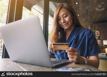 A beautiful asian woman holding credit cards while using laptop computer