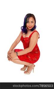A beautiful Asian woman in a red dress and high heels crouching on thefloor in the studio, isolated for white background.