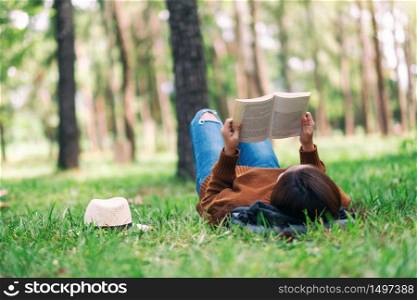 A beautiful Asian woman lying and reading a book in the park