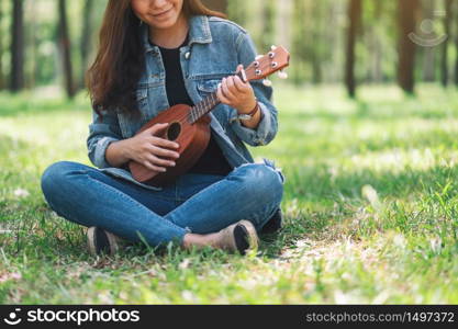 A beautiful asian woman sitting and playing ukulele in the outdoors