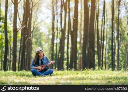 A beautiful asian woman sitting and playing ukulele in the outdoors