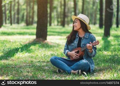 A beautiful asian woman sitting and playing ukulele in the park