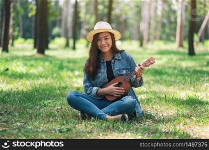 A beautiful asian woman sitting and playing ukulele in the park