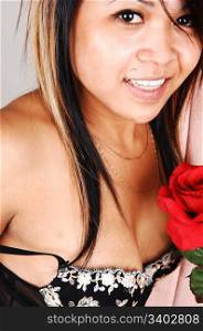 A beautiful Asian woman sitting in the studio for a portrait with a redrose in her hand, in black lingerie and nice smile, light gray background.