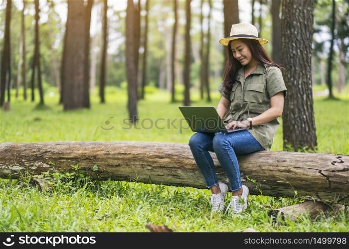 A beautiful asian woman using and typing on laptop keyboard while sitting on a log in the park