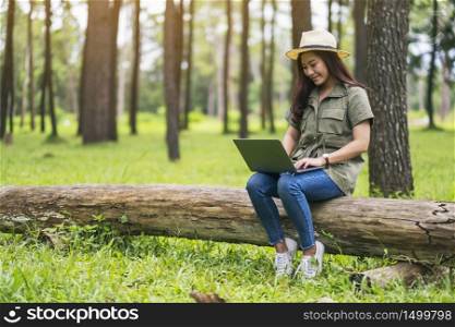 A beautiful asian woman using and typing on laptop keyboard while sitting on a log in the park