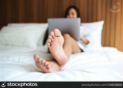 A beautiful asian woman using and working on laptop computer while lying on a white cozy bed at home