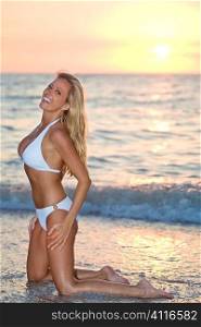 A beautiful bikini clad blond kneeling in the surf at sunset