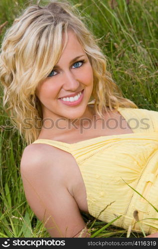 A beautiful blond haired blue eyed model laying down amid tall grass