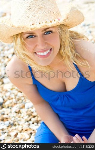 A beautiful blond haired blue eyed model wearing a straw cowboy hat and with a gorgeous smile shot in close up at the beach and illuminated with natural light