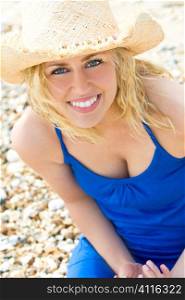 A beautiful blond haired blue eyed model wearing a straw cowboy hat and with a gorgeous smile shot in close up at the beach and illuminated with natural light