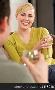 A beautiful blond haired blue eyed young woman drinking water and smiling while on a date with a young man who is out of focus in the forground