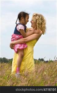 A beautiful blond haired blue eyed young woman having fun in a field of long grass with her mixed race young daughter