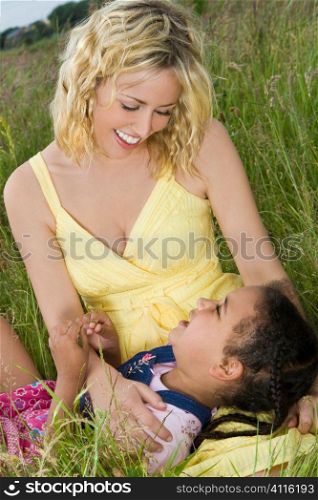 A beautiful blond haired blue eyed young woman having fun with a mixed race little girl in a field of long grass