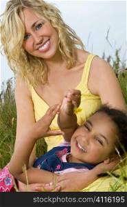 A beautiful blond haired blue eyed young woman having fun with a mixed race young girl in a field of long grass