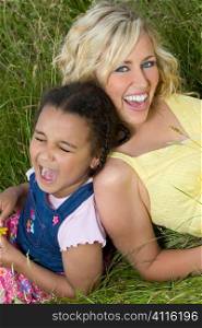 A beautiful blond haired blue eyed young woman having fun with a mixed race young girl in a field of long grass