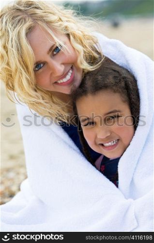 A beautiful blond haired blue eyed young woman keeping herself and her young daughter warm in a towel at the beach