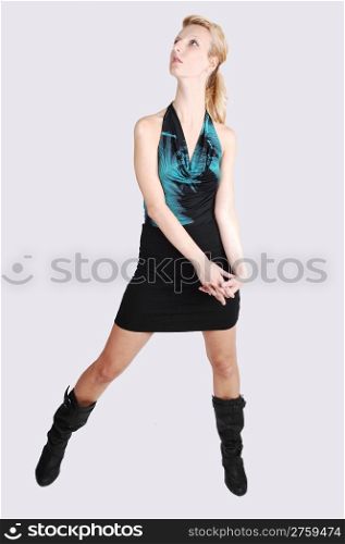 A beautiful blond tall woman standing in the studio in a black skirt and bootslooking up to the sealing, for light gray background.
