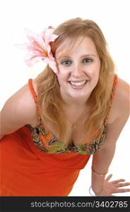 A beautiful blond teenager sitting on the floor, smiling into the camera witha pink lily in her hair and in a colorful orange dress, for white background.