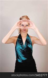 A beautiful blond woman holding her hands before her eyes and makinga sign, like a photographer, what the picture will look like, over light graybackground.