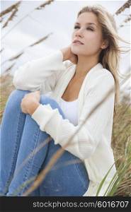 A beautiful blond woman or girl wearing jeans siiting in tall grass on a beach