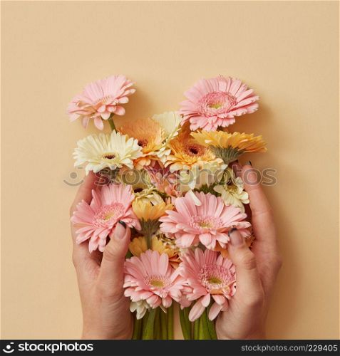 A beautiful bouquet of orange, white and pink gerberas the girl is holding in hands on a yellow paper background. as a greeting card for Valentine's Day or Mother's Day. Flat lay. A beautiful bouquet of gerbera the girl is holding in hands on a yellow paper background.
