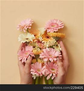A beautiful bouquet of orange, white and pink gerberas the girl is holding in hands on a yellow paper background. as a greeting card for Valentine's Day or Mother's Day. Flat lay. A beautiful bouquet of gerbera the girl is holding in hands on a yellow paper background.