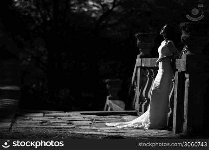 A beautiful bride in a luxurious dress stands on a large balcony. Black and white photo.. A beautiful bride in a luxurious dress stands on a large balcony. Black and white photo